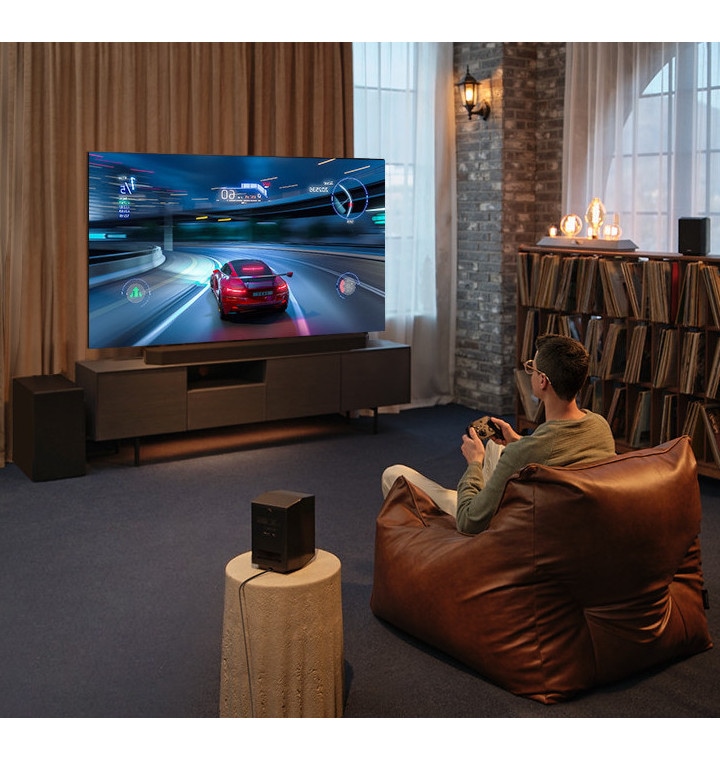 Man sitting on a couch in a loungeroom playing video games on a big screen TV