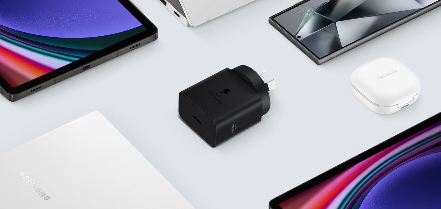 A top view of various Samsung Galaxy devices are shown with a black Power Adapter placed at the center. To the left, a Galaxy Book3, to the right Galaxy Buds2 Pro in White, a Galaxy Tab S9 and Galaxy S24 Ultra are also shown.
