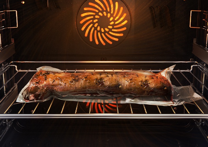 Shows a joint of meat inside the oven, which is tightly sealed in a plastic bag and on a metal tray, being cooked using the Air Sous Vide system.