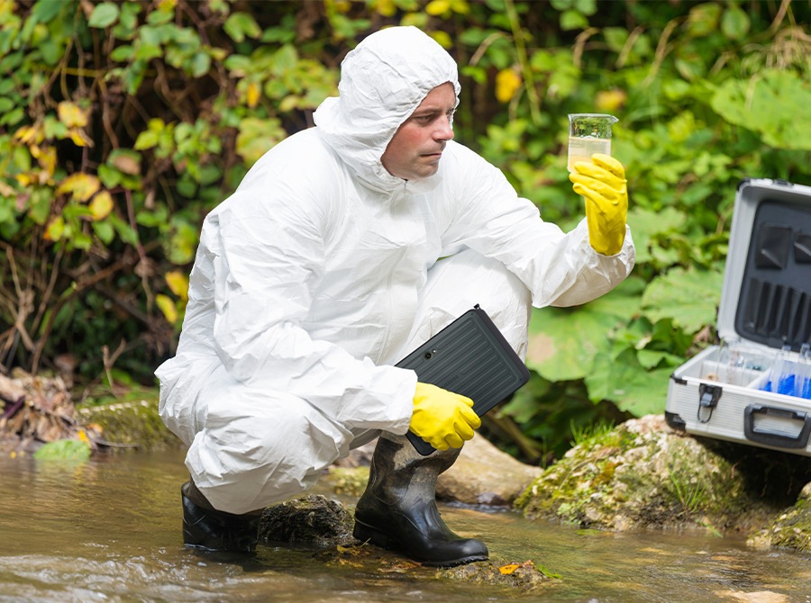 A man in a lab coat and protective gear holds Galaxy Tab Active5 Pro while collecting water samples by a lake, illustrating the device’s resistance to water, dust and dirt.