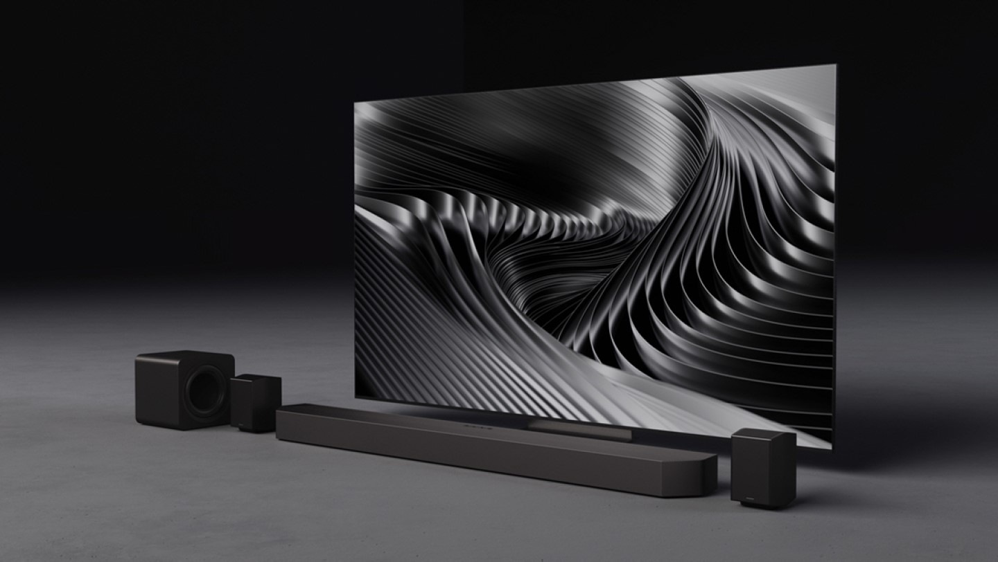 Samsung presents Q-Series Soundbar Q990F. Q990F below TV in a room. Q990F inner components are shown. Soundwaves show 11.1.4ch fully immersive surround sound that envelops you. Subwoofer inner components are shown. Inside the powerful 8-inch dual active subwoofer, AI-powered nonlinear control technology is enabled. Soundwaves play from subwoofer. Rear speaker inner components are shown and soundwaves show upfiring channels. Soundwaves in various directions show Wireless Dolby Atmos with Dolby Atmos logo. Cable between TV and soundbar disappears. Immersive sound without an HDMI cable. TV & Soundbar speakers work together in perfect harmony with Q-Symphony. SpaceFit Sound Pro analyzes the room for stunning sound automatically tuned and calibrated for your space. Active Voice Amplifier pro boosts voices based on outside noise and in-content audio. Catch every word without distraction. Adaptive Sound plays sound and dialogue optimized for your content. Q990F setup with TV. Samsung logo.