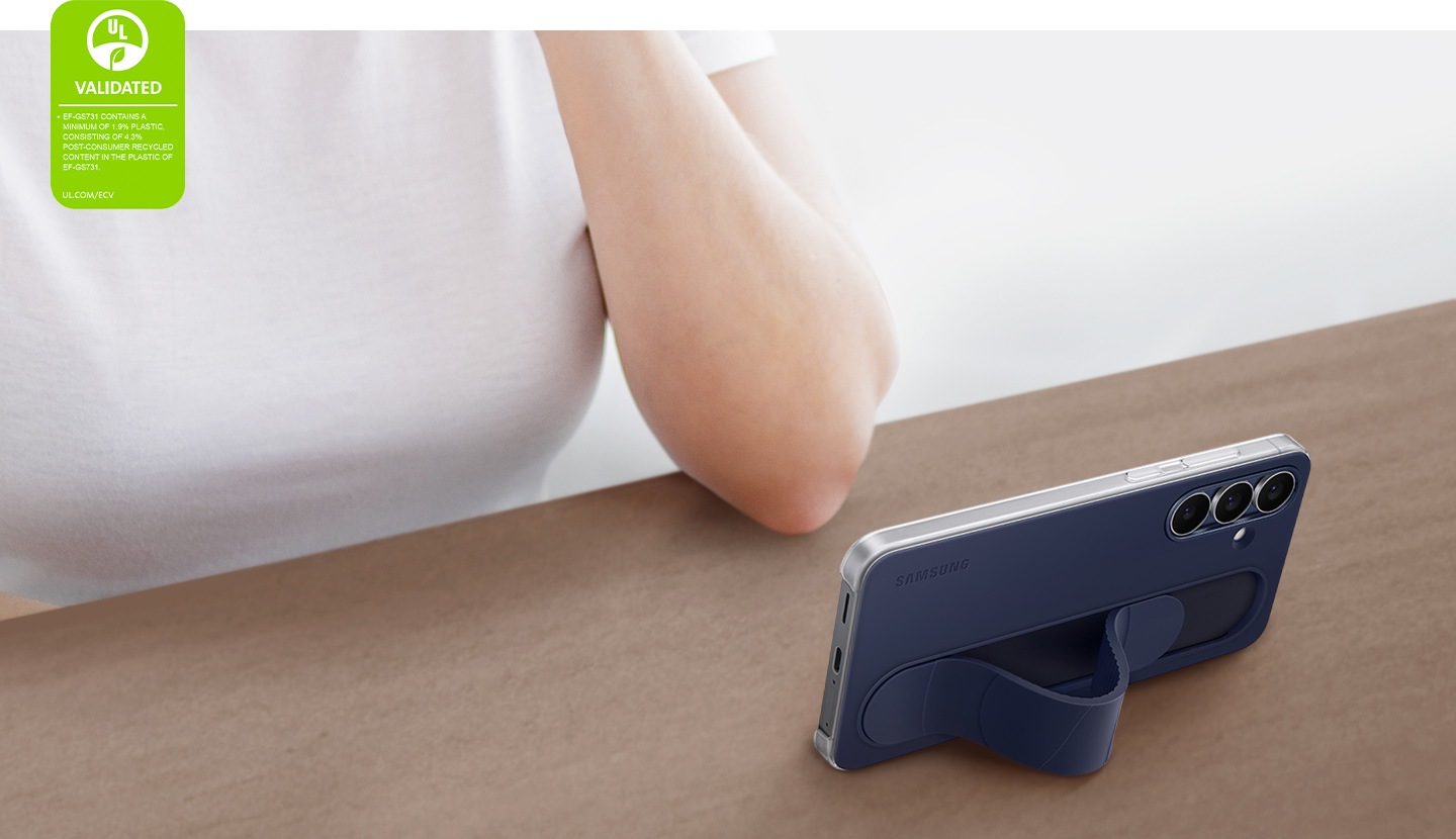 A Galaxy S25 FE encased in the Standing Grip Case in Dark Blue stands horizontally in a slanted angle on a table. The phone is being used by a person for viewing purposes.