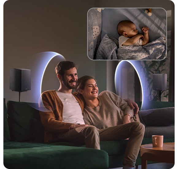 Couple sitting on sofa receive sound waves from rear speakers placed around them. In another space, a baby sleeps in a crib.