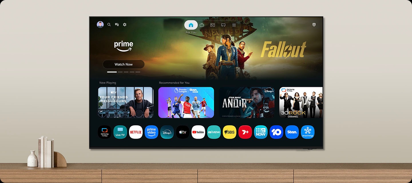 One UI Tizen’s home screen, with the various apps and services available, is displayed on a TV in a living room.