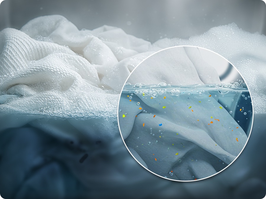 The laundry is immersed in foamy water. A close-up shows microplastic fragments in the water. The ‘Less Microfiber cycle' course reduces microplastics up to 54%. 