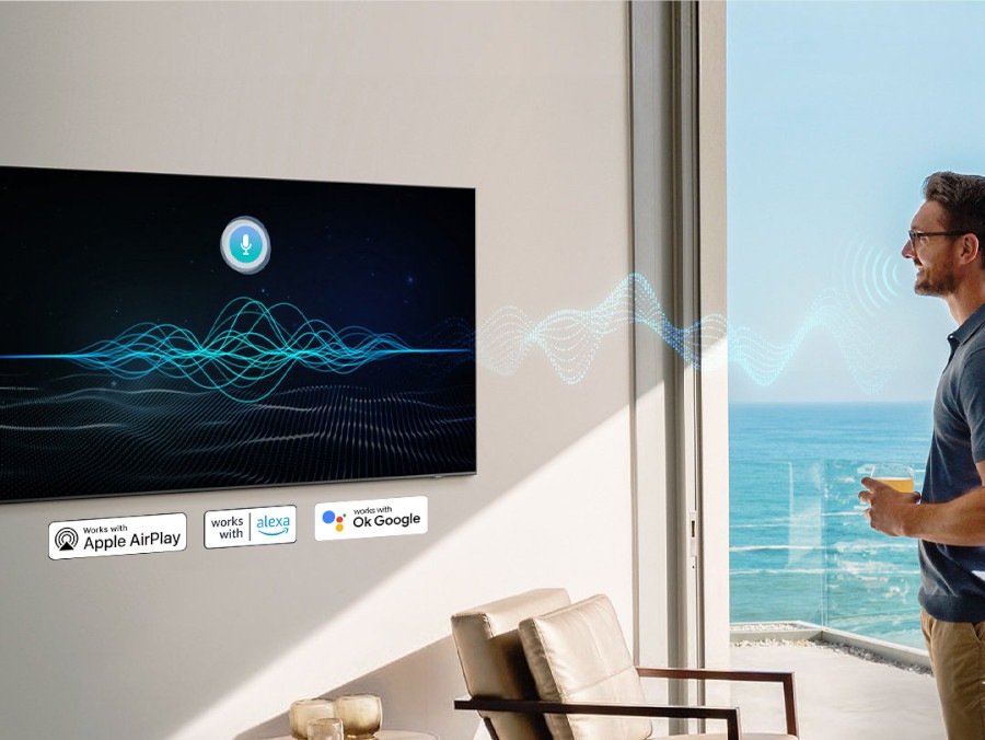 A man talking to his TV with voice activation logos underneath for apple airplay, ok google and amazon Alexa