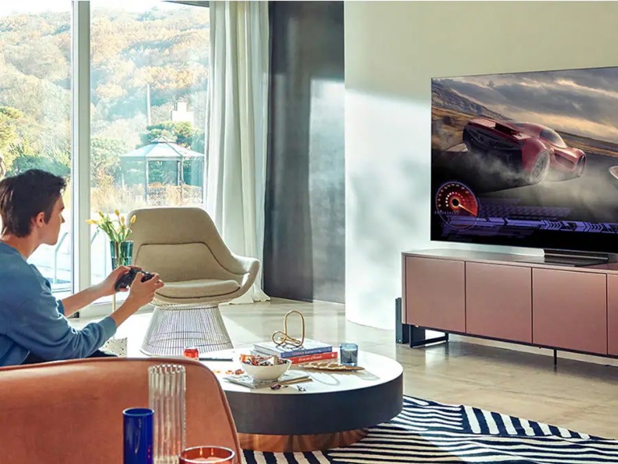 igralec, ki igra video igro avtomobilskih dirk 4K v dnevni sobi na televizorju Samsung s svetlobo, ki prihaja skozi okno