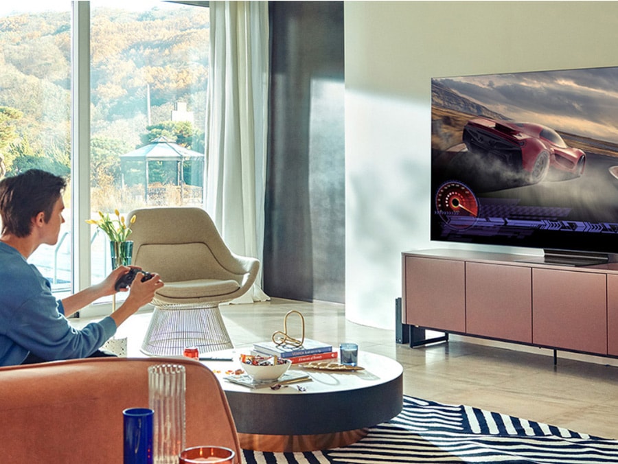 A man playing a racing game on large screen TV in a living room