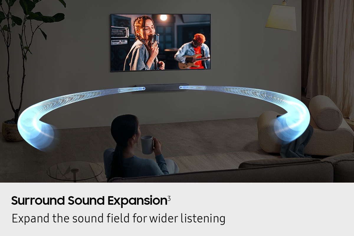 A woman watches TV in a living room. Sound waves shoot out from the soundbar and travel in various directions to surround her.