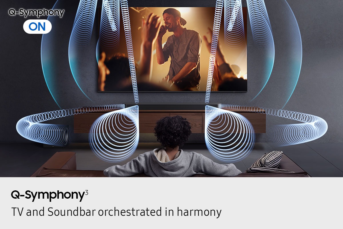 Man watches TV in living room. With Q-Symphony ON, sound plays from Q990F soundbar and TV, shown by various sound waves.
