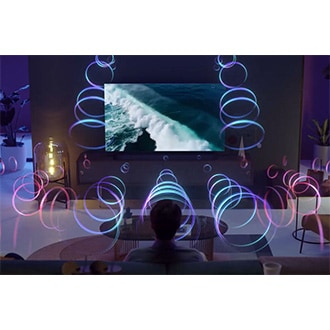 A man is watching a Samsung TV as Q-symphony synchronizes audio from both the TV and Soundbar without muting TV speakers.
