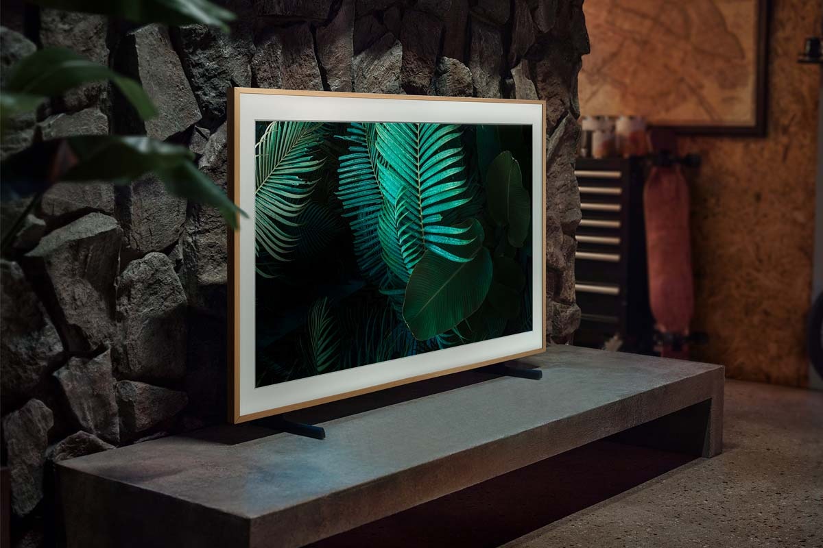 The Frame TV is mounted on the Adjustable Height Stand accessory on top of a TV cabinet in a dimly lit room and is displaying the image of a green fern.