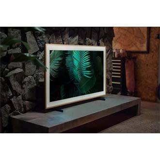 The Frame TV is mounted on the Adjustable Height Stand accessory on top of a TV cabinet in a dimly lit room and is displaying the image of a green fern.