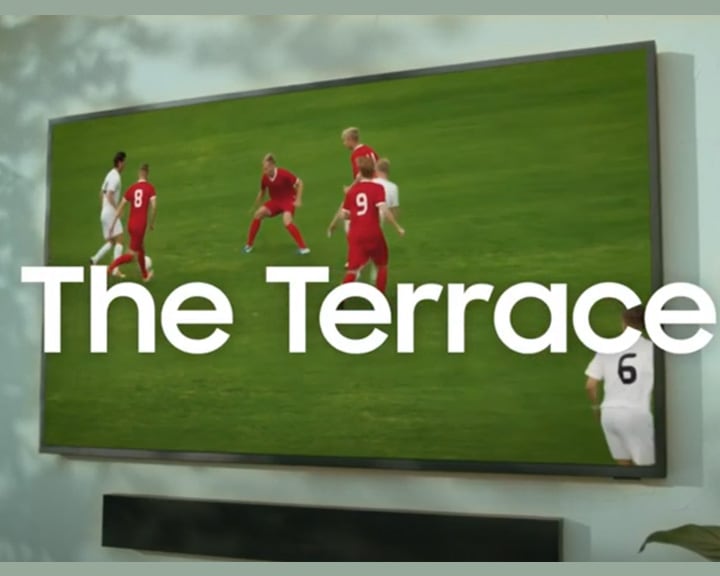 A man is outside watching the football on The Terrace Outdoor TV that is mounted to the wall undercover.