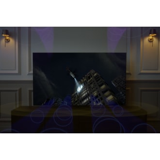 A Neo QLED TV is displaying a helicopter shooting light onto a building at night. Sound waves from its top channel speakers is filling the room.