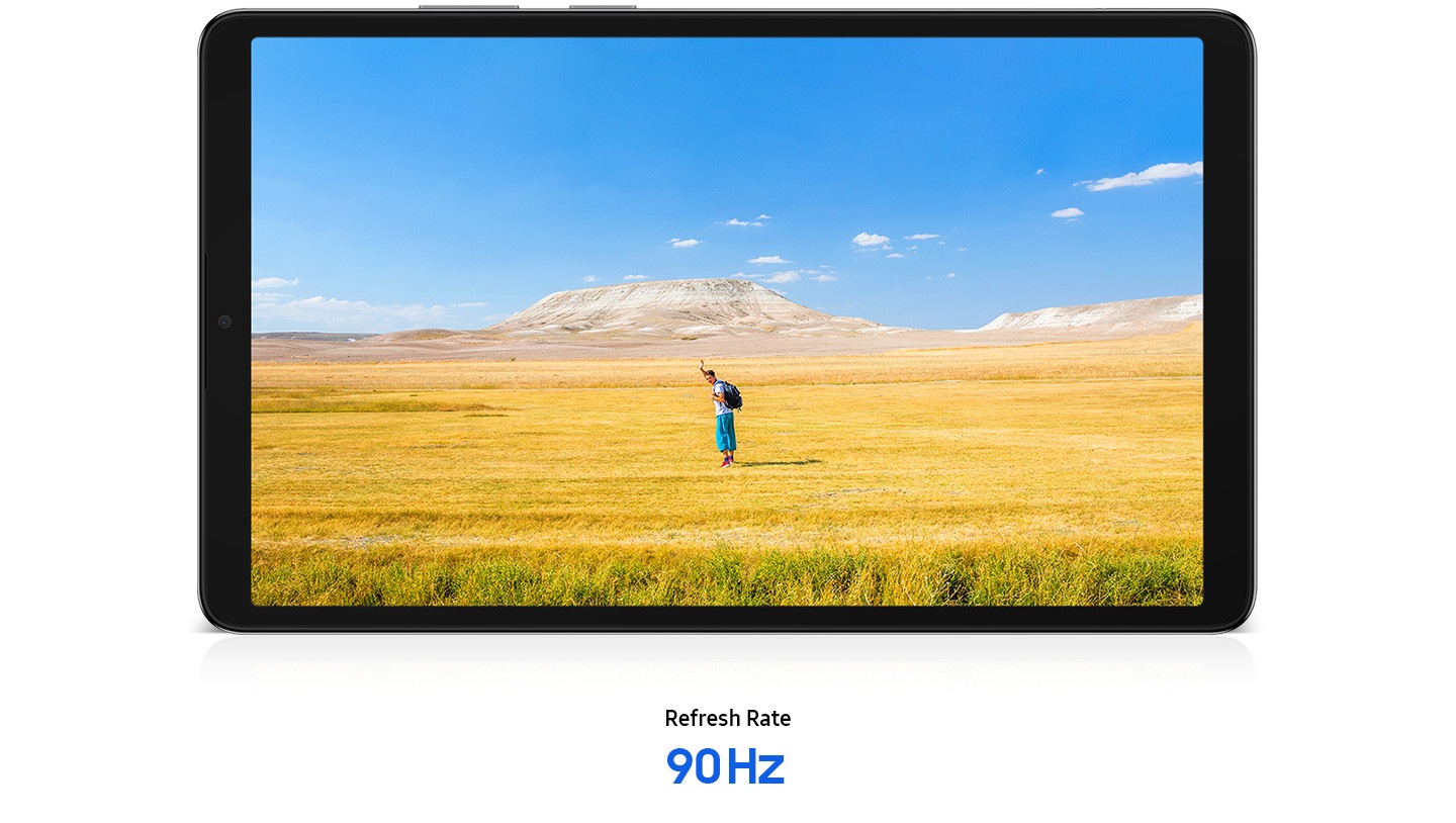 Galaxy Tab A11 is placed horizontally, displaying a clear image of a man waving his hands, suggesting a free-spirited mood. In the background, a blue sky stretches over a wide horizon of yellow and brown grass. Below the tablet, text reads ‘Refresh Rate 90 Hz’.