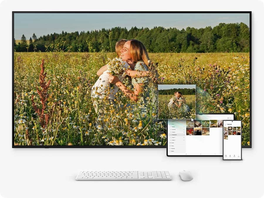 A connected mouse and keyboard move a photo from a tablet, synced to a smartphone gallery, onto a TV using drag-and-drop.
