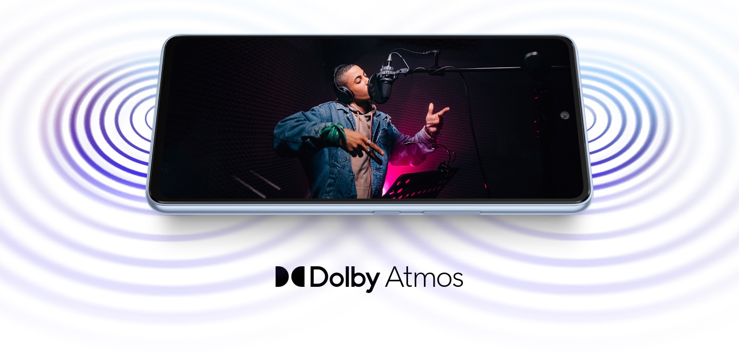 Le Galaxy A53 5G est posé horizontalement et montre le son provenant des deux extrémités de l'appareil. À l'écran, un artiste masculin portant des écouteurs chante dans un micro de studio lors d'une session d'enregistrement. Le logo Dolby Atmos apparaît en dessous.