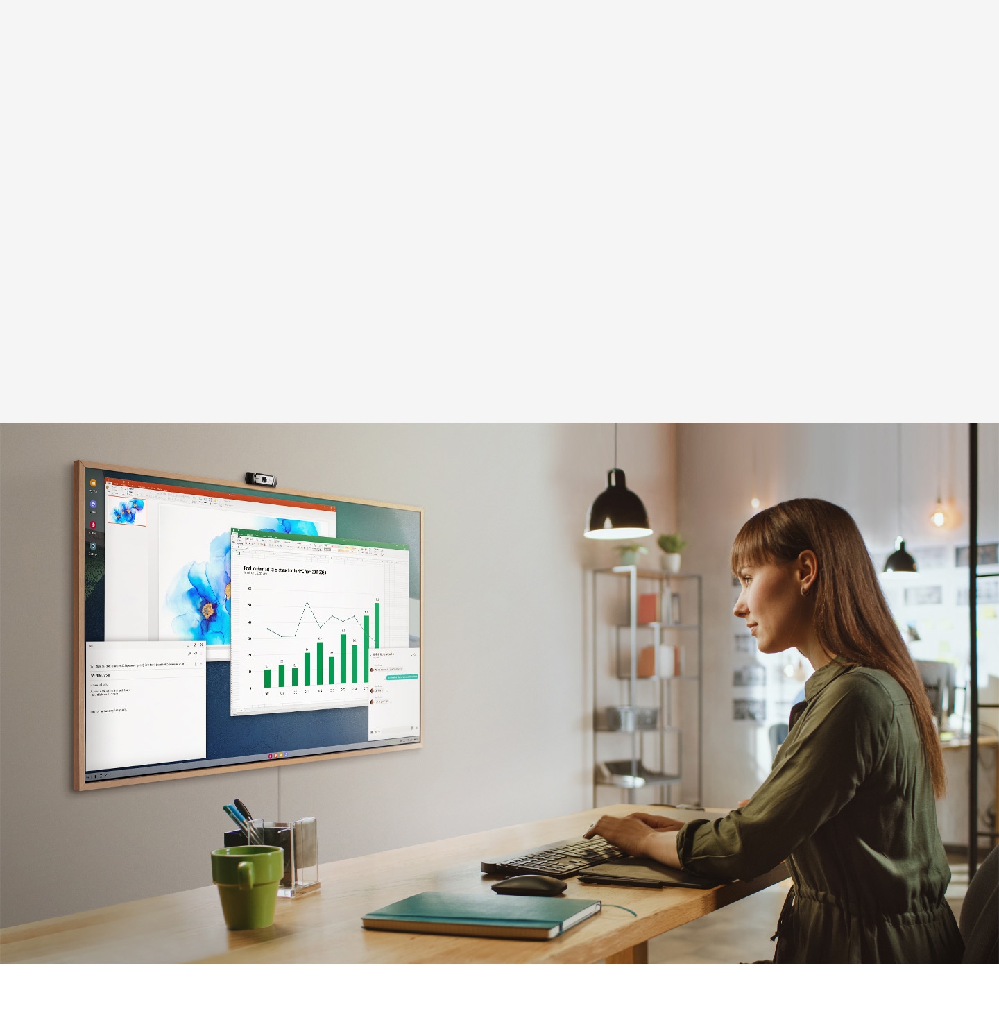 Ženska uporablja svoj pisarniški računalnik za delo na televizijskem zaslonu doma.  Na zaslonu okvirja so različna pisarniška okna produktivnosti.