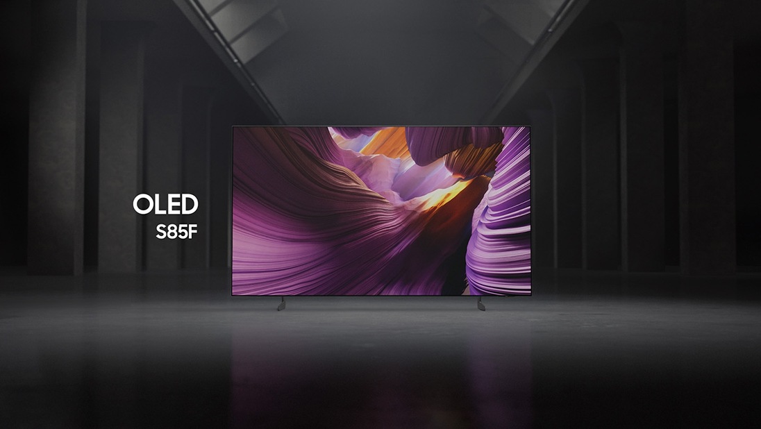 Le téléviseur Samsung OLED S85F, dans un espace intérieur noir et blanc, affiche une scène colorée représentant un paysage d'un autre monde.