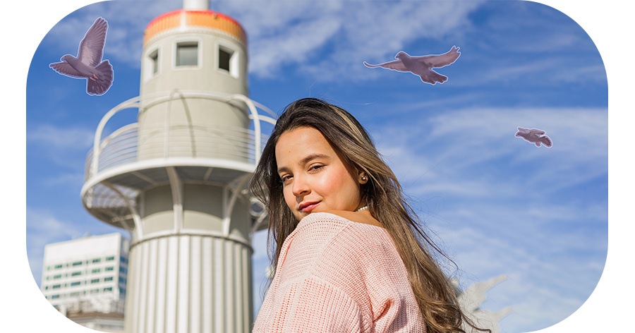 Uma fotografia no modo retrato de uma mulher olhando para trás na câmera com um pássaro voando ao fundo no céu azul. Quando o apagador de objetos é aplicado, o pássaro é apagado do fundo. 