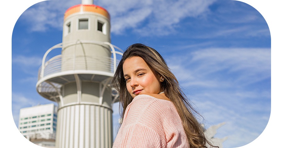 Uma fotografia no modo retrato de uma mulher olhando para trás na câmera com um pássaro voando ao fundo no céu azul. Quando o apagador de objetos é aplicado, o pássaro é apagado do fundo. 