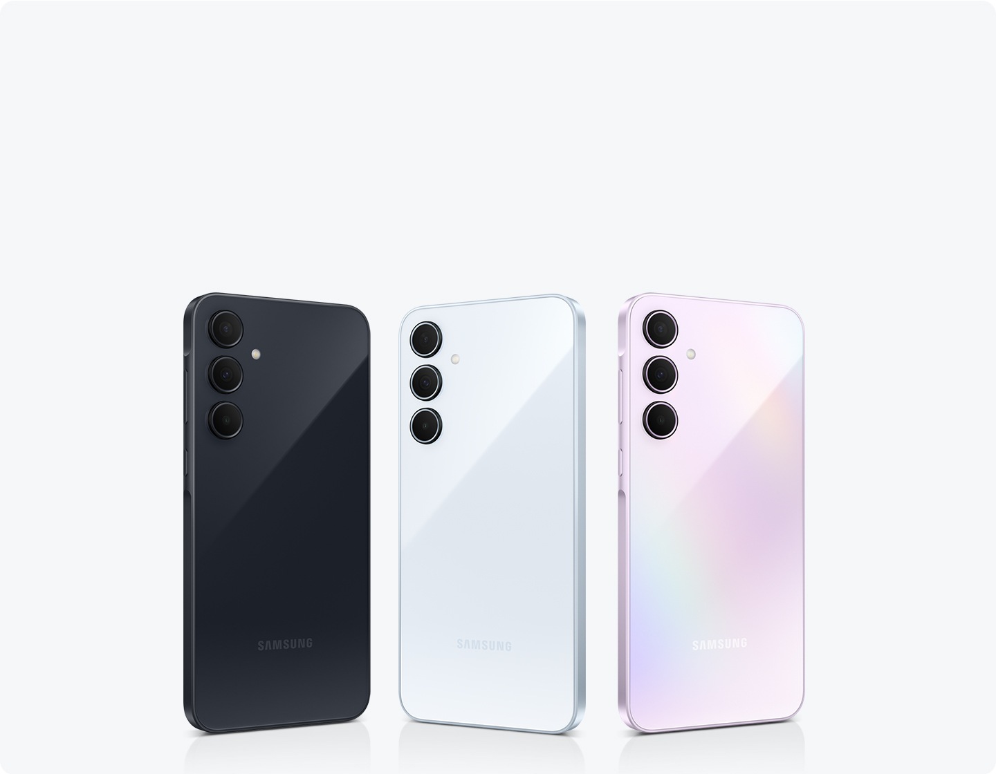 Três smartphones Samsung perfilados com cores variadas: Azul Claro, Rosa e Azul Escuro. Cada celular apresenta um layout de três câmeras na parte traseira.