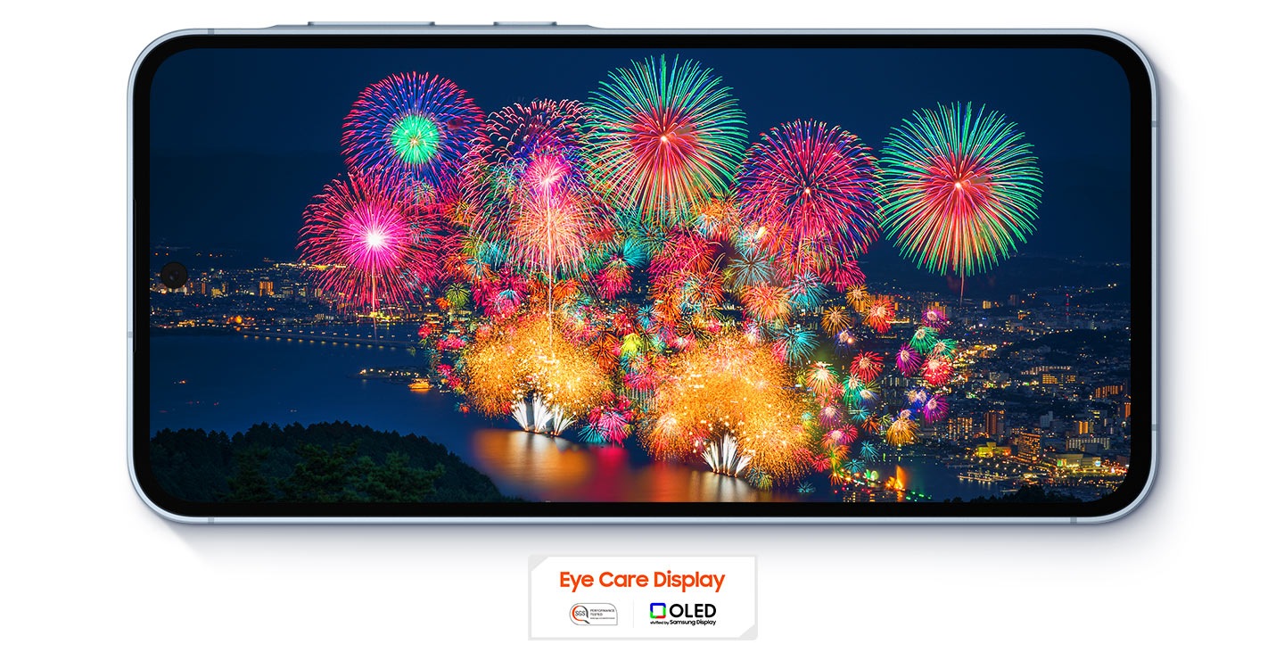 Fogos de artifício vibrantes surgem sobre uma paisagem urbana, vistos em um Galaxy A55 5G no Modo Paisagem. Com os logotipos Eye Care Display e tecnologia OLED embaixo do celular.