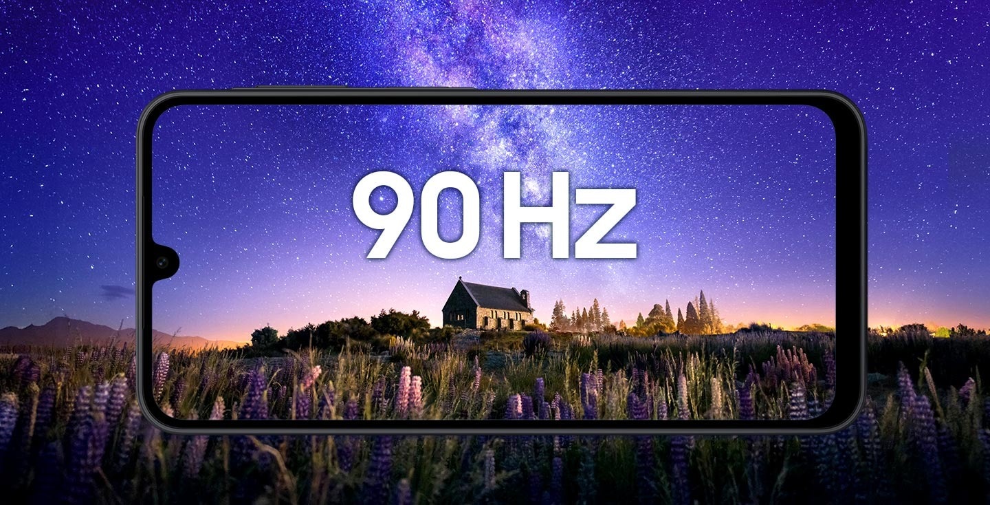 Visão horizontal de um Galaxy A17 preto mostrando uma cena noturna: uma casa de pedra cercada por flores roxas sob um céu estrelado em tons violeta-azulados. No centro da tela, o texto “90 Hz” destaca a fluidez da taxa de atualização.