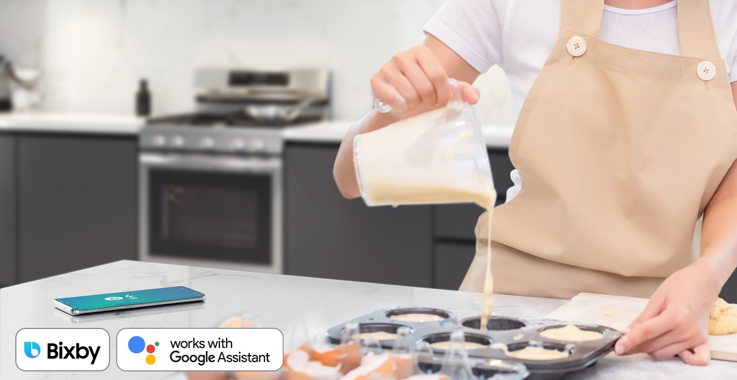 Shows a person baking while controlling the oven with their voice using a smartphone app, such as Bixby and Google Assistant.