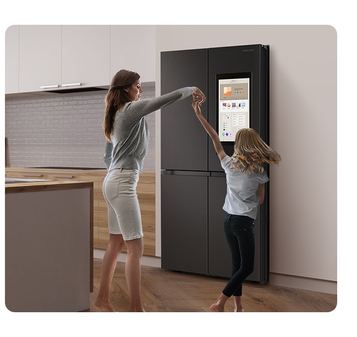 A mother dances with her child in a stylish kitchen in front of a Family Hub. The display has a music app and a playlist.