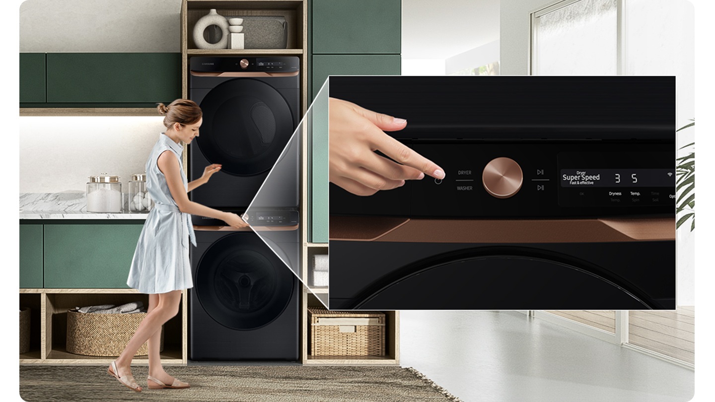 A woman controls the dryer stacked on top of the washer by touching the washer panel underneath.