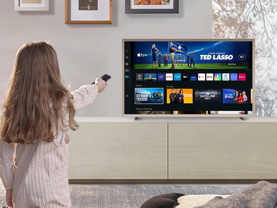 A girl is pointing the remote towards The Frame, which shows the Smart Hub home screen.