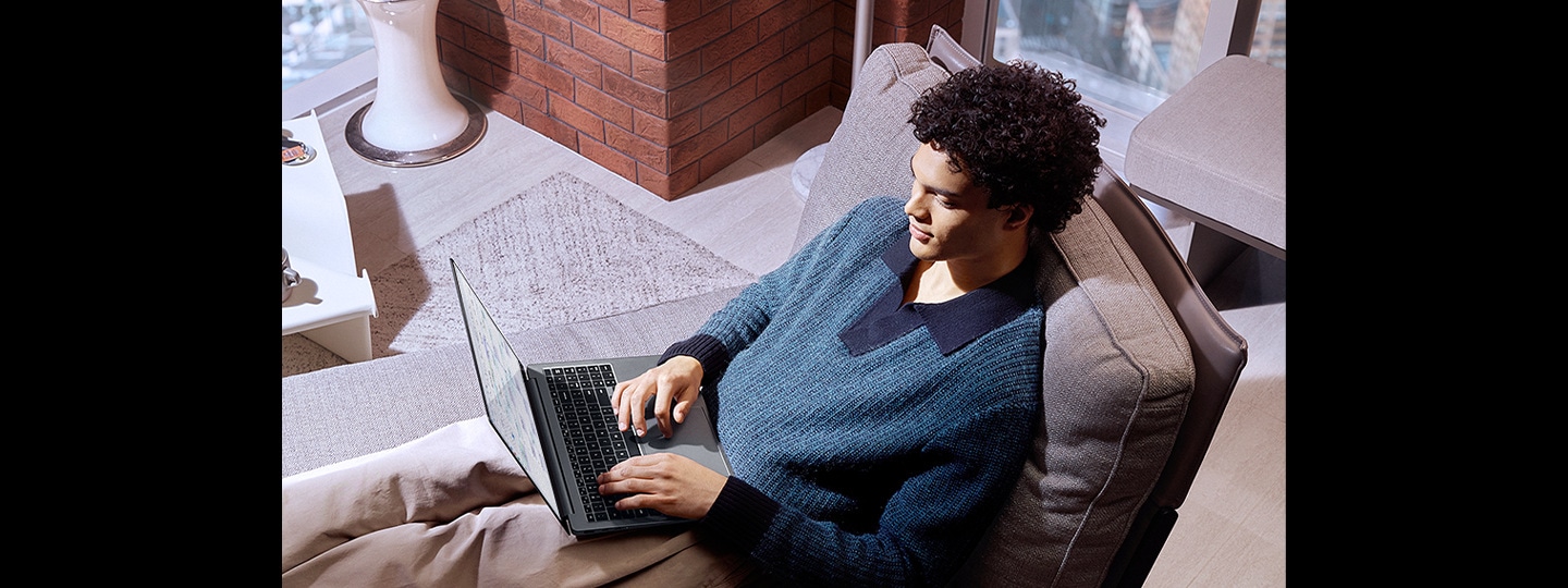 A young man reclining comfortably on a couch is using Galaxy Book4 Ultra in Moonstone Gray without worries that the battery will run out.