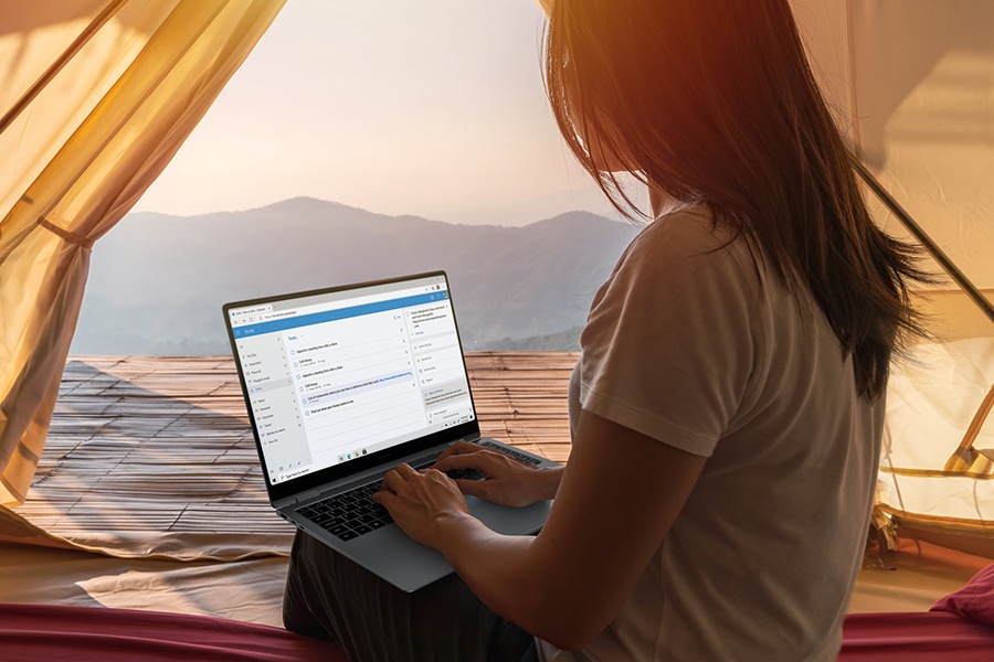 A woman is using Galaxy Book5 Pro 360 with Microsoft Outlook app open onscreen without a charger worry-free in a tent outdoors.