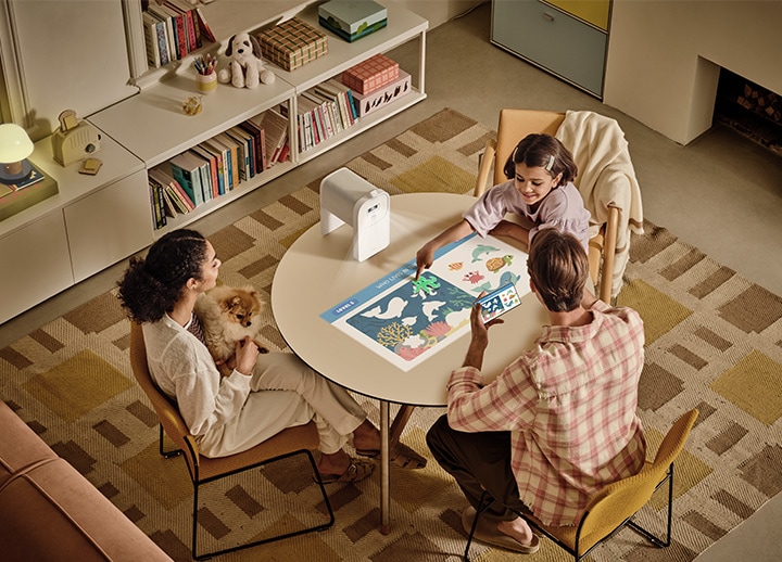 A parent and child play a mobile game projected onto the table by The Premiere, mirrored directly from a smartphone.