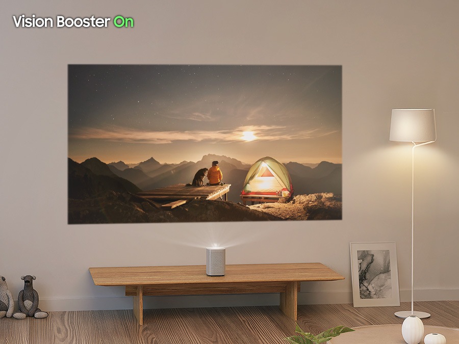 The Premiere projects an image of campers enjoying a sunset onto the wall of a living room. A nearby lamp floods the screen with brightness. With Vision Boost Off, the image is vague and hard to see. With Vision Boost On, the image clears up significantly.