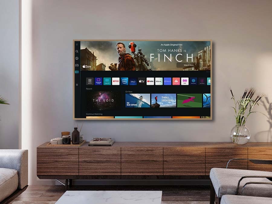A Girl is Specing the Remote Towards The Frame, Which Shows The Smart Hum Home Screen