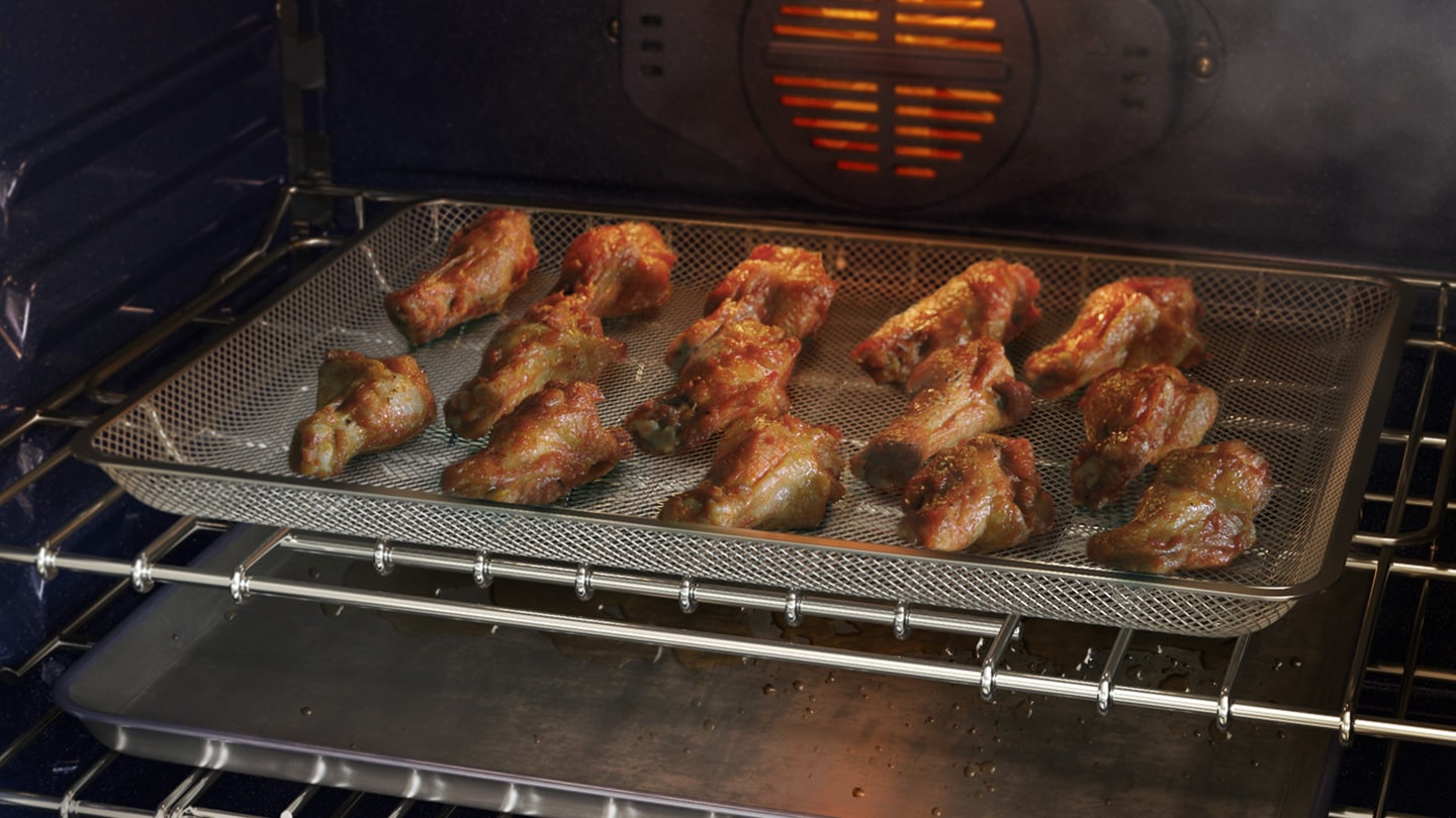 It shows chicken wings being cooked inside an air fryer-specific tray, with oil dripping down to the bottom.