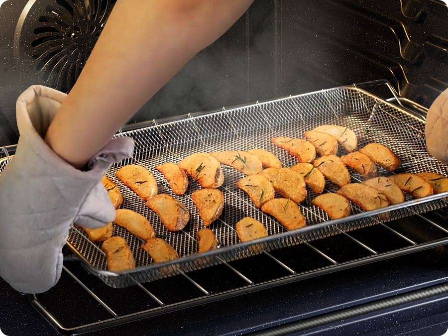 Two hands wearing oven mitts are taking out a tray of potatoes from an oven with the Air Fry featured turned off.