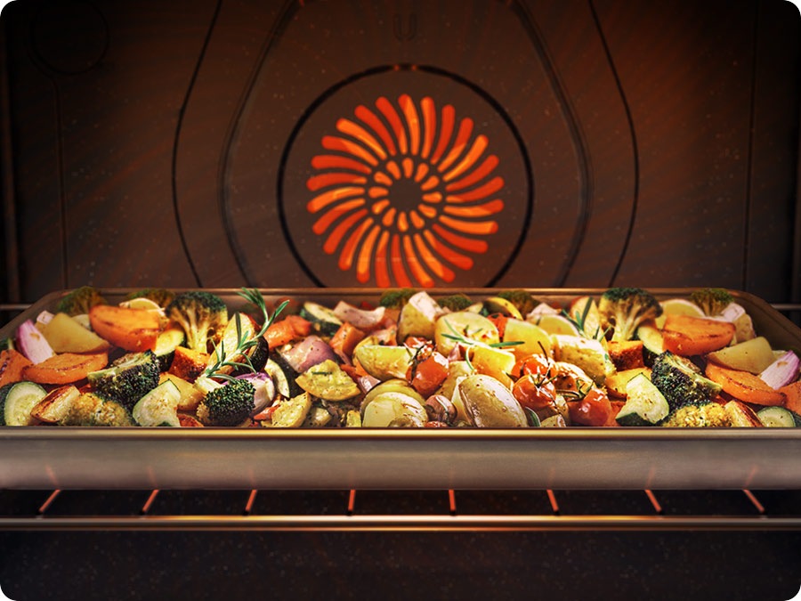 An oven pan filled with various herbs and vegetables is cooking in the oven. They are evenly cooked.