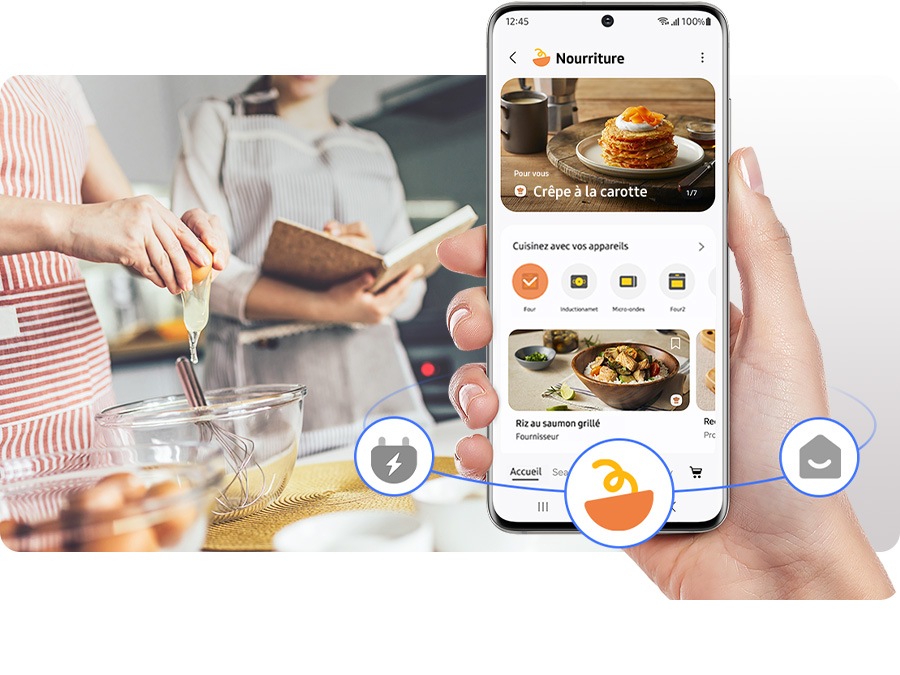 A hand holds a mobile phone with SmartThings onscreen, giving real-time cooking updates from an induction range in a kitchen.