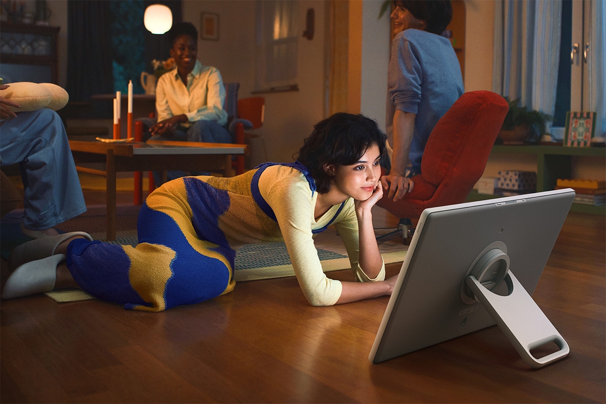 Une femme regarde du contenu sur The Movingstyle, posé sur sa béquille intégrée, alors qu’elle est assise par terre.