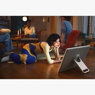 Une femme regarde du contenu sur The Movingstyle, posé sur sa béquille intégrée, alors qu’elle est assise par terre.