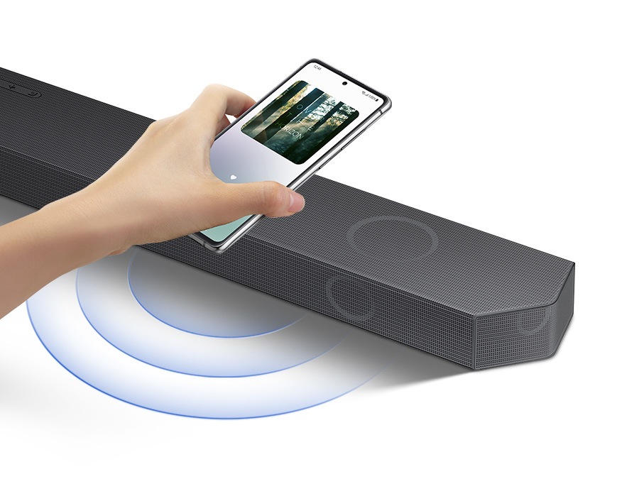 Uma mão toca um smartphone com o aplicativo de música Samsung na tela na barra de som e a barra de som toca instantaneamente música, mostrando como é fácil mudar do smartphone para a barra de som