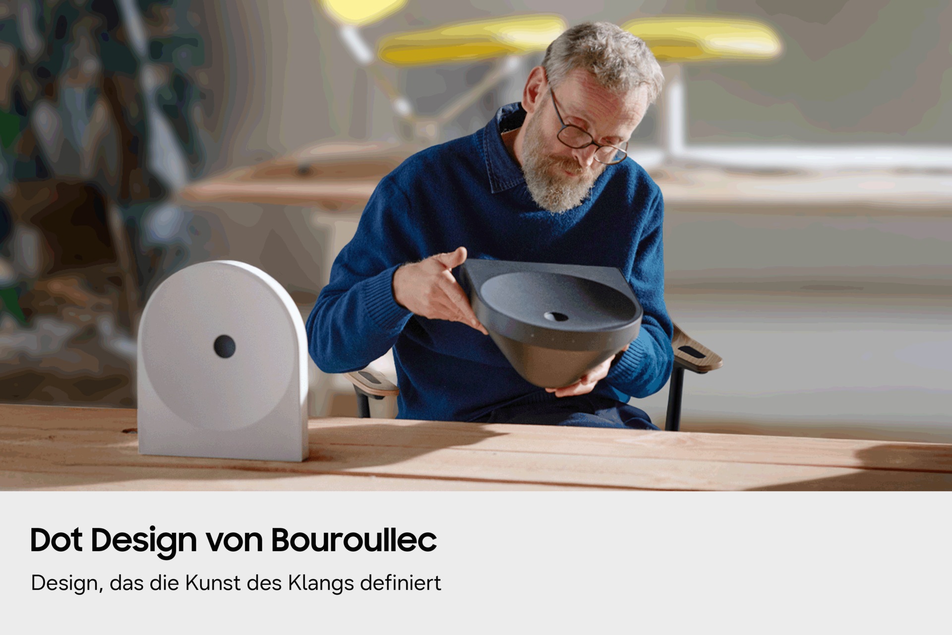 Erwan Bouroullec hält einen Samsung-Lautsprecher in der Hand und betrachtet dessen Design. Davor steht ein weiterer Samsung-Lautsprecher. 