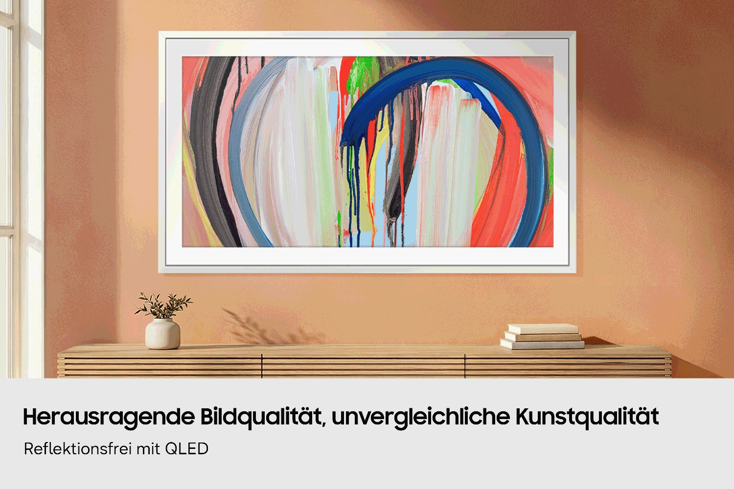 An einer  Wand hängt ein Samsung Frame TV, auf dem ein Gemälde mit Pinselstrichen zu sehen ist; darunter steht eine schlichte Holzkonsole mit einer kleinen Pflanze und Büchern.