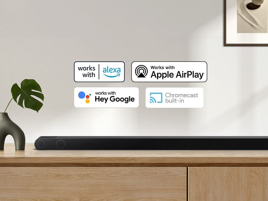 Логотип Alexa, логотип Apple AirPlay, Hey Google Logo та вбудований логотип Chromecast разом із звуковою панеллю Samsung S800B, яка сидить на шафі вітальні
