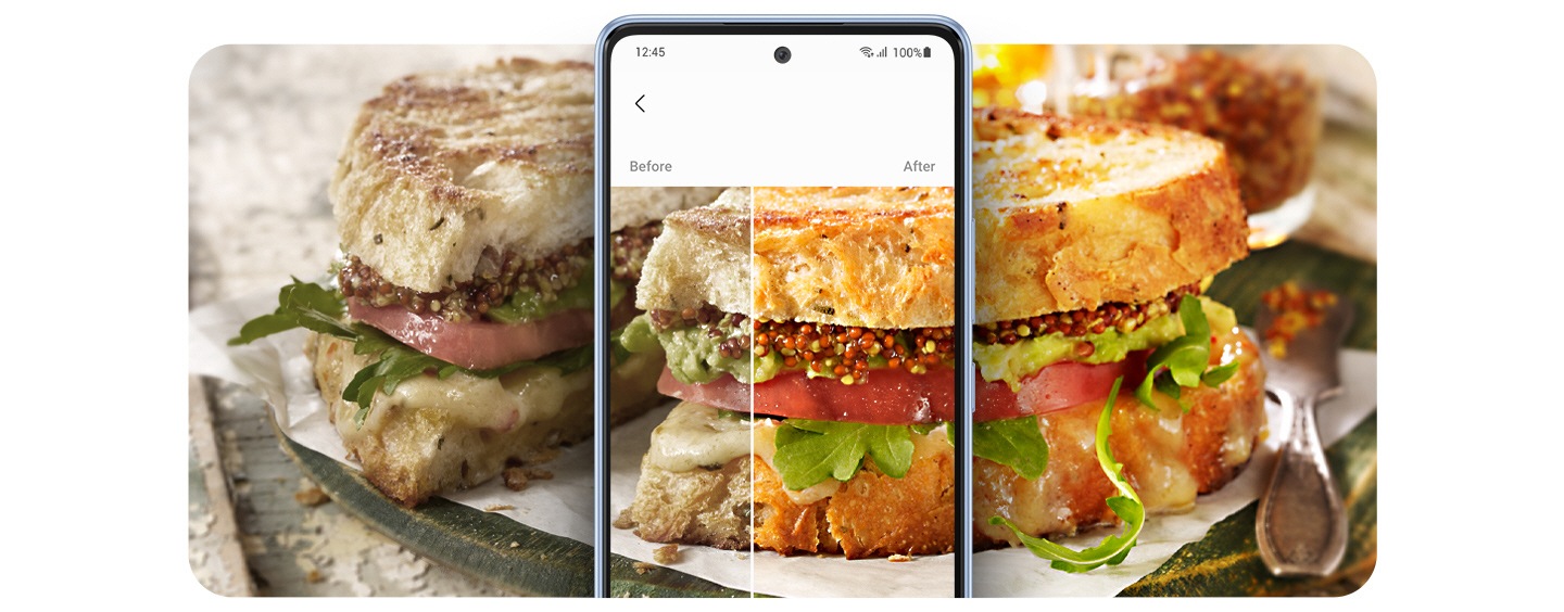 Se muestra una foto ancha de un plato de un sándwich rebanado, diseccionado por un Galaxy A53 5G en el centro. A la izquierda del teléfono inteligente, la imagen del sándwich está poco atractiva y silenciada. A la derecha, la otra mitad del sándwich se muestra mucho más brillante, colorida y apetitosa. En la pantalla, el sándwich también se corta con los efectos Antes y Después del Remaster fotográfico, mostrando la diferencia en la calidad de la imagen. 