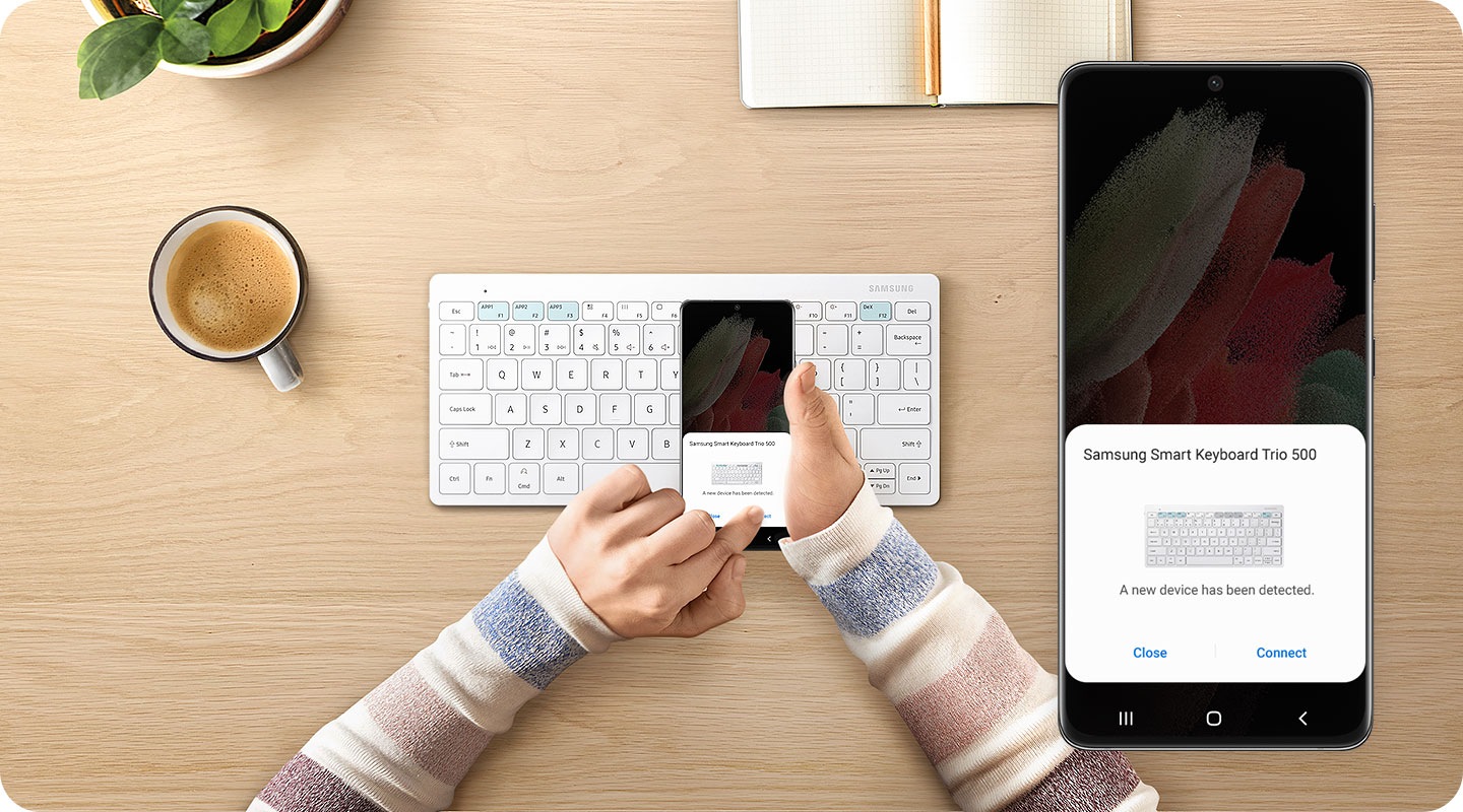 There is a white-colored Samsung Smart Keyboard Trio 500 on a desk. Above it, two hands are holding a smartphone, on which it shows the easy pairing pop-up. A left hand is pressing the †connect' button of the pop-up. On the right side, there is a close-up of what is onscreen on the phone.